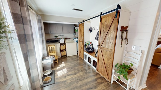 mudroom featuring crown molding, dark wood finished floors, visible vents, a barn door, and washer and dryer