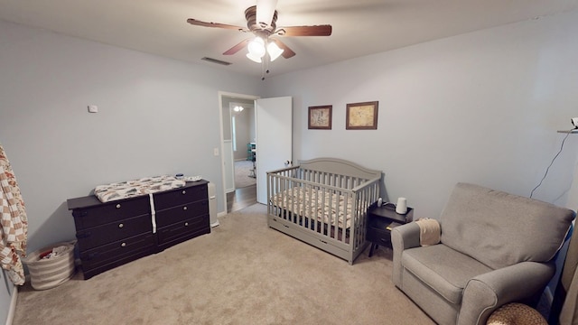 carpeted bedroom featuring a crib, visible vents, and a ceiling fan