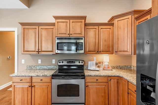 328 Hidden Creek Cir, Dothan, AL 36301 - kitchen featuring stainless steel appliances, light wood finished floors, light stone counters, and brown cabinets