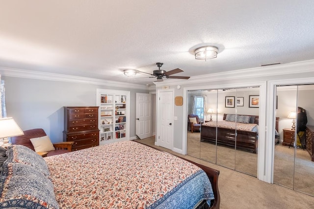 carpeted bedroom featuring a textured ceiling, ceiling fan, crown molding, and two closets