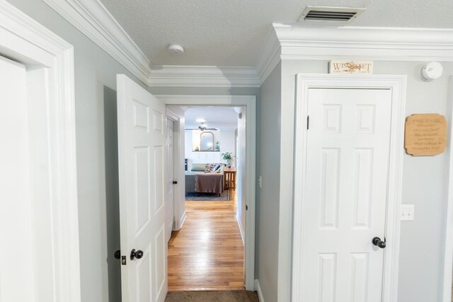 corridor featuring hardwood / wood-style flooring, crown molding, and a textured ceiling