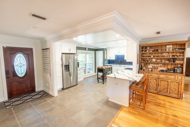 kitchen with backsplash, stainless steel refrigerator with ice dispenser, light hardwood / wood-style flooring, white cabinetry, and a breakfast bar area