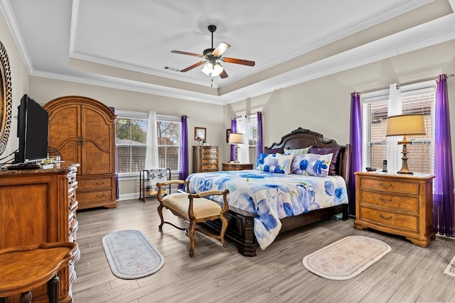 bedroom with ornamental molding, ceiling fan, a tray ceiling, and light hardwood / wood-style flooring