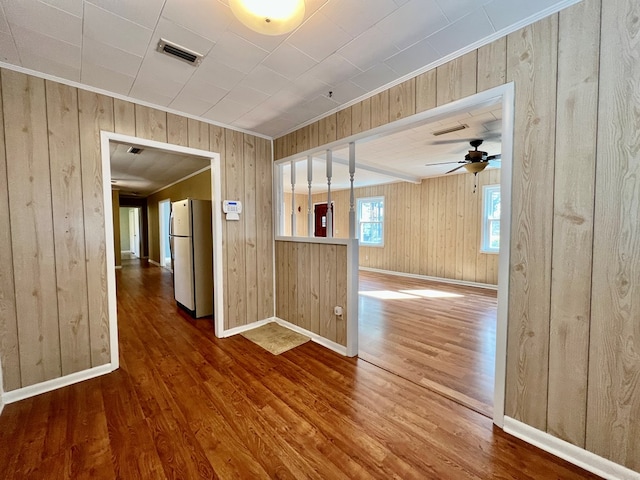 spare room with wood-type flooring, ornamental molding, ceiling fan, and wood walls