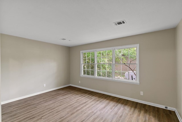 empty room with baseboards, visible vents, and wood finished floors