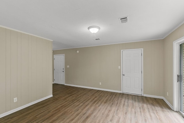 empty room with visible vents, wood finished floors, baseboards, and ornamental molding
