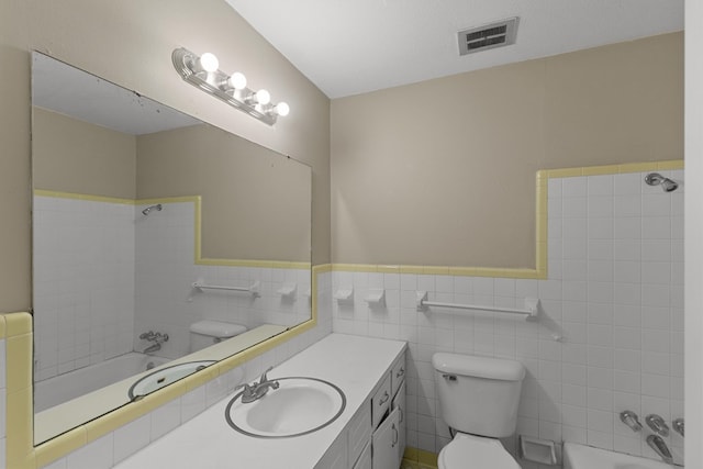 full bath with toilet, bathtub / shower combination, a wainscoted wall, visible vents, and vanity