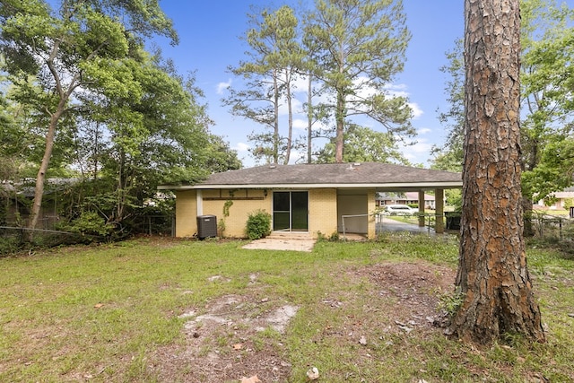 rear view of property with a lawn, brick siding, fence, central AC unit, and an attached carport