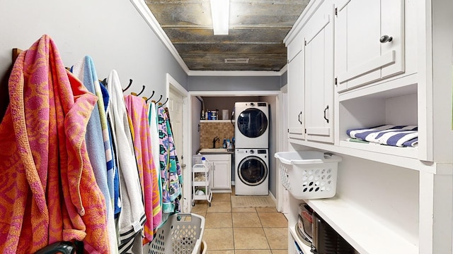 clothes washing area featuring light tile patterned floors, sink, cabinets, stacked washer / dryer, and ornamental molding