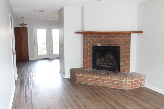 unfurnished living room featuring dark wood-type flooring, a textured ceiling, and a brick fireplace