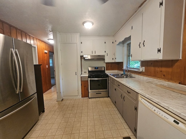 kitchen with stainless steel appliances, under cabinet range hood, light countertops, a sink, and wooden walls