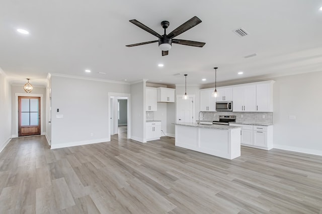 kitchen with appliances with stainless steel finishes, white cabinetry, a kitchen island with sink, tasteful backsplash, and light stone countertops