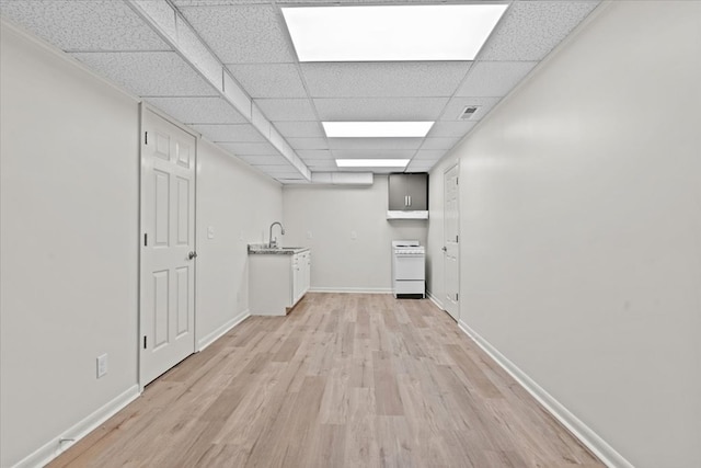 empty room with light wood-type flooring, a paneled ceiling, baseboards, and a sink
