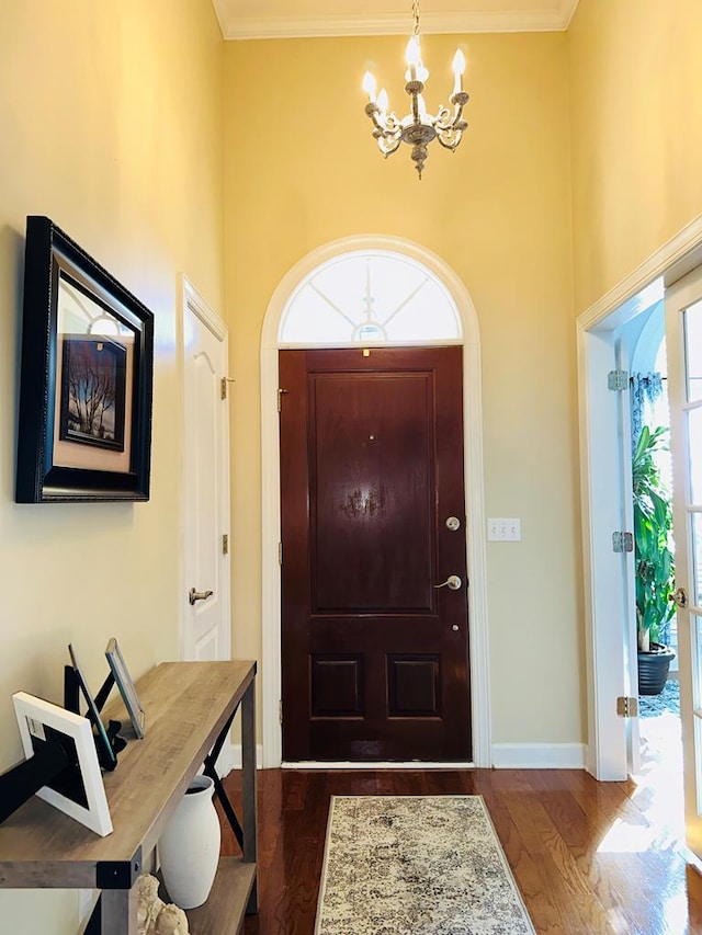 entryway featuring a chandelier, a towering ceiling, dark wood-type flooring, and ornamental molding