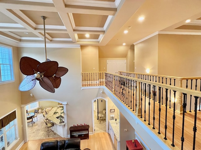 interior space with coffered ceiling, light hardwood / wood-style flooring, a high ceiling, and ornamental molding