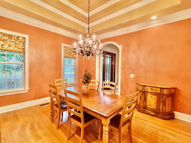 dining space with wood-type flooring, an inviting chandelier, a raised ceiling, and crown molding