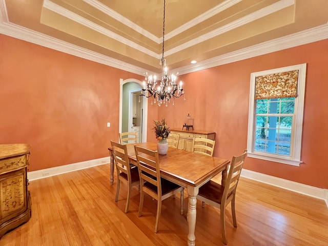 dining space with light wood-type flooring, a tray ceiling, and ornamental molding