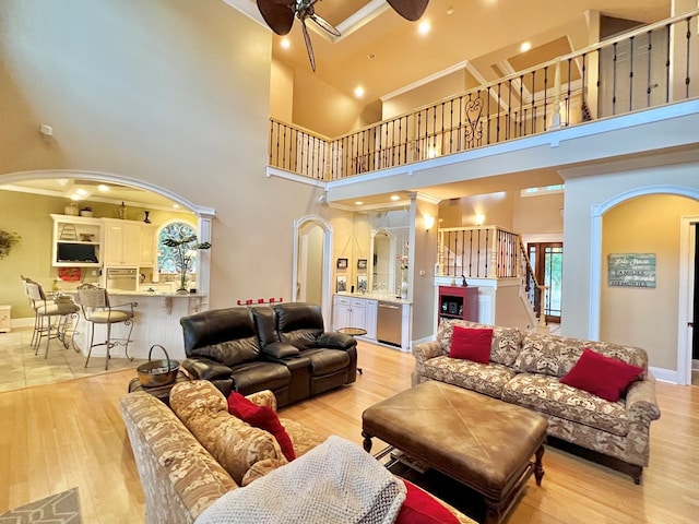 living room featuring ceiling fan, a towering ceiling, ornamental molding, and light hardwood / wood-style flooring