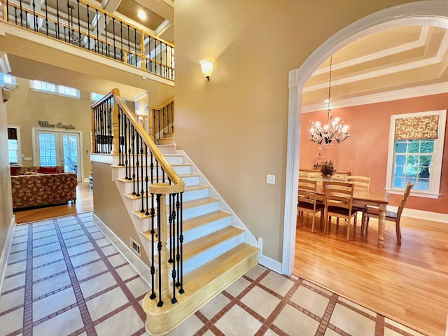 stairway with french doors, a high ceiling, a notable chandelier, crown molding, and wood-type flooring