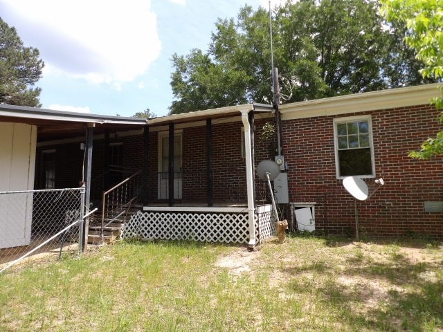 rear view of property featuring a lawn, covered porch, and brick siding