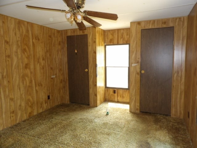 carpeted empty room featuring a ceiling fan and wooden walls