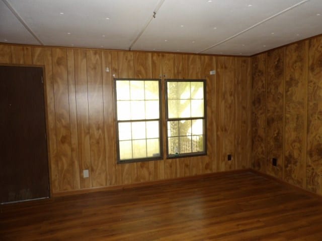 spare room with wood walls, wood finished floors, and baseboards