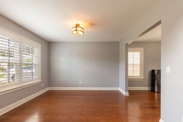 spare room featuring baseboards, dark wood-style floors, and a wealth of natural light