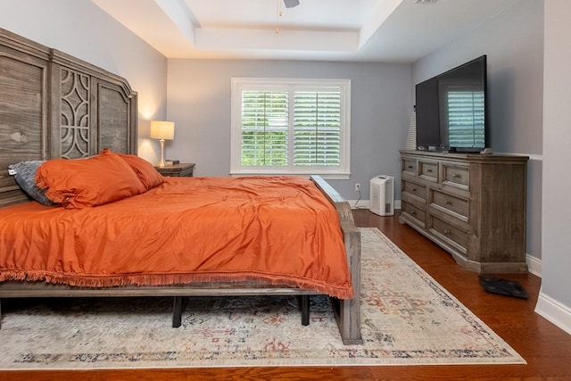 bedroom featuring baseboards, a raised ceiling, and dark wood-type flooring