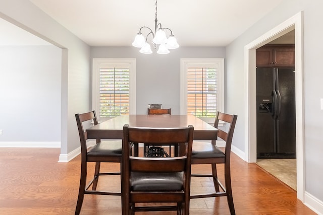 dining space with baseboards, plenty of natural light, light wood-type flooring, and a notable chandelier