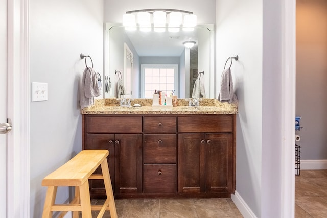 full bathroom featuring baseboards, double vanity, and a sink