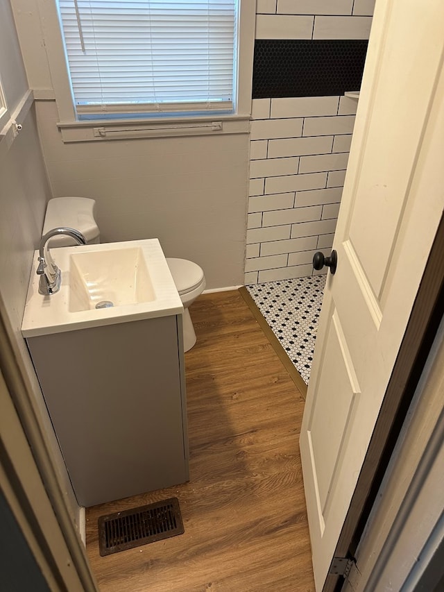 bathroom with vanity, hardwood / wood-style flooring, toilet, walk in shower, and tile walls