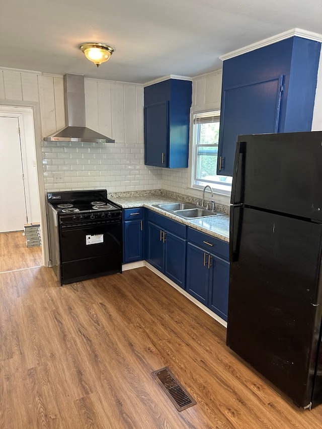 kitchen with wall chimney range hood, blue cabinets, light hardwood / wood-style floors, decorative backsplash, and black appliances