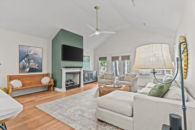 living area with a fireplace, a ceiling fan, baseboards, wood finished floors, and vaulted ceiling