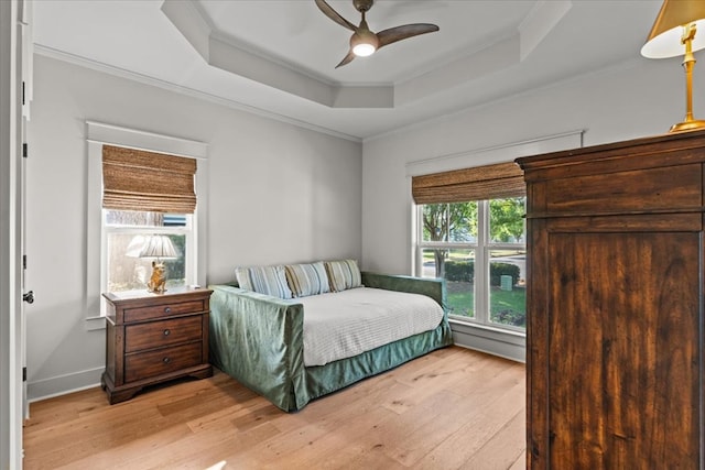 bedroom featuring light wood-style floors, a raised ceiling, ornamental molding, and ceiling fan