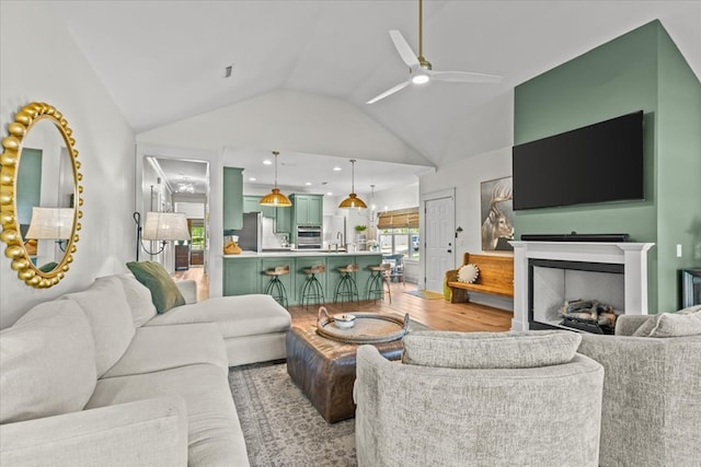 living room featuring light wood finished floors, ceiling fan, vaulted ceiling, and a fireplace