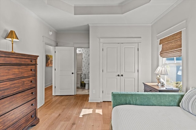 bedroom featuring a closet, ornamental molding, light wood-type flooring, connected bathroom, and a tray ceiling
