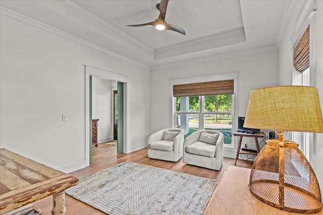 living area featuring ornamental molding, wood finished floors, baseboards, ceiling fan, and a tray ceiling