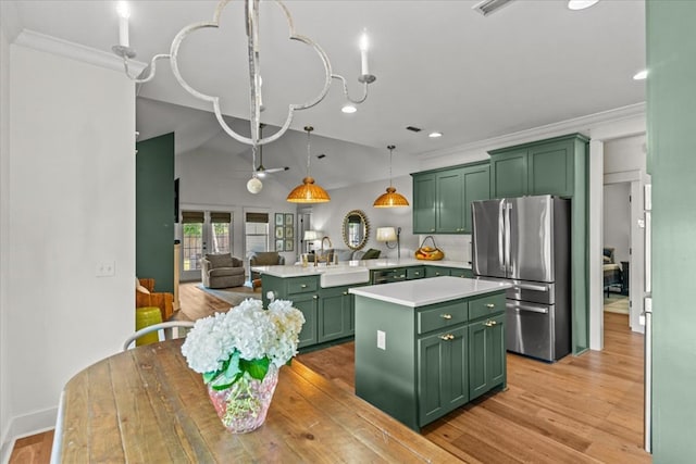 kitchen featuring light countertops, a sink, freestanding refrigerator, a peninsula, and green cabinetry