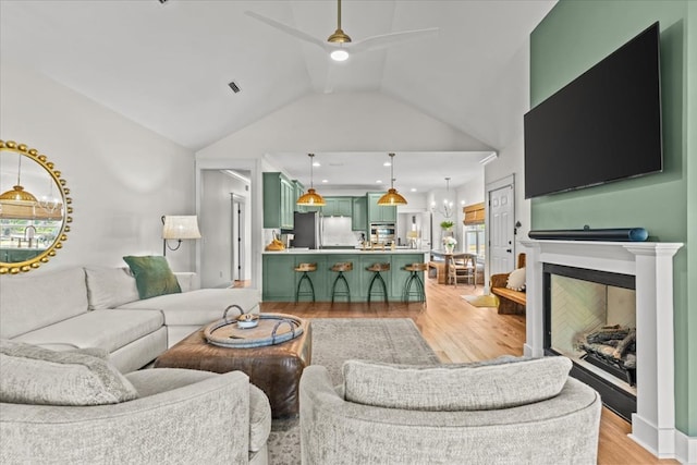 living area with ceiling fan, light wood-style flooring, lofted ceiling, and a fireplace