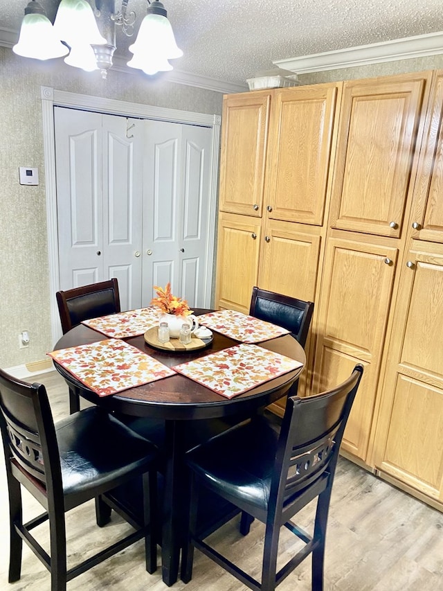 dining space featuring light hardwood / wood-style floors, a textured ceiling, and ornamental molding