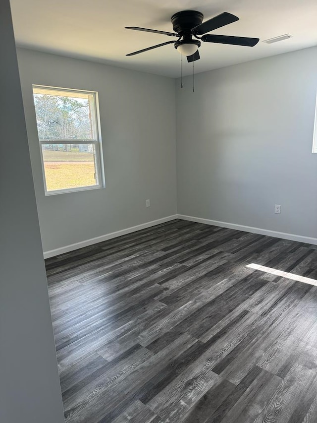 empty room with ceiling fan, dark wood finished floors, visible vents, and baseboards