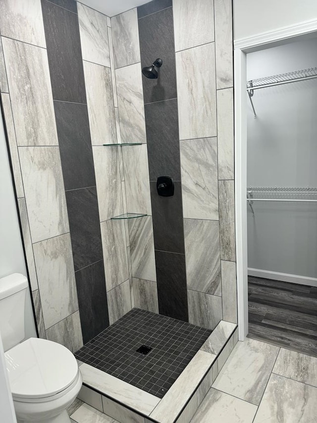 bathroom featuring marble finish floor, a spacious closet, a shower stall, and toilet