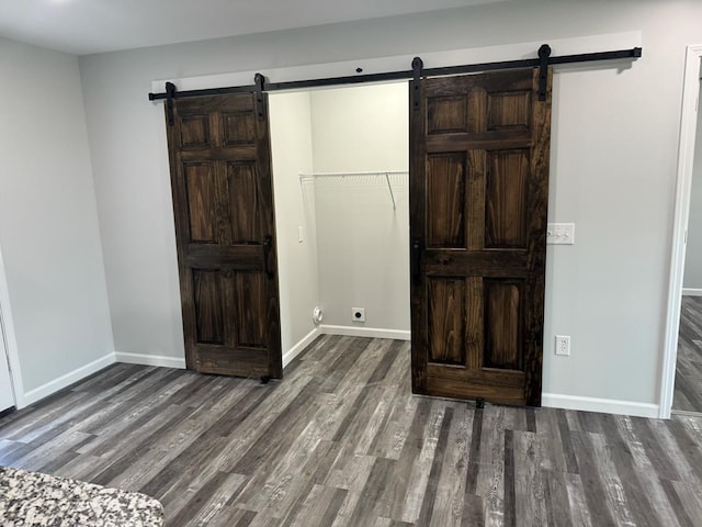 unfurnished bedroom featuring wood finished floors, baseboards, and a barn door