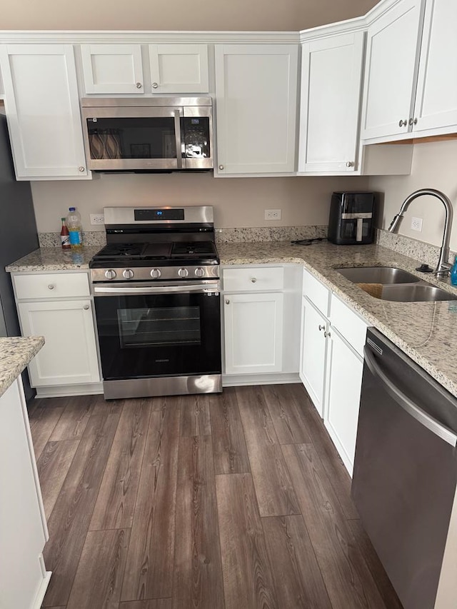 kitchen featuring stainless steel appliances, light stone countertops, dark hardwood / wood-style flooring, sink, and white cabinetry