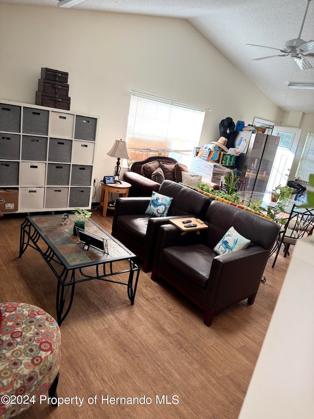 living room featuring light wood-type flooring, vaulted ceiling, ceiling fan, and a textured ceiling