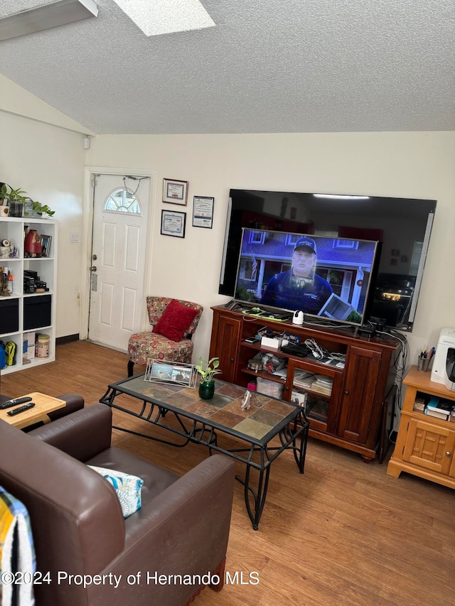 living room with lofted ceiling with skylight, light wood-type flooring, and a textured ceiling