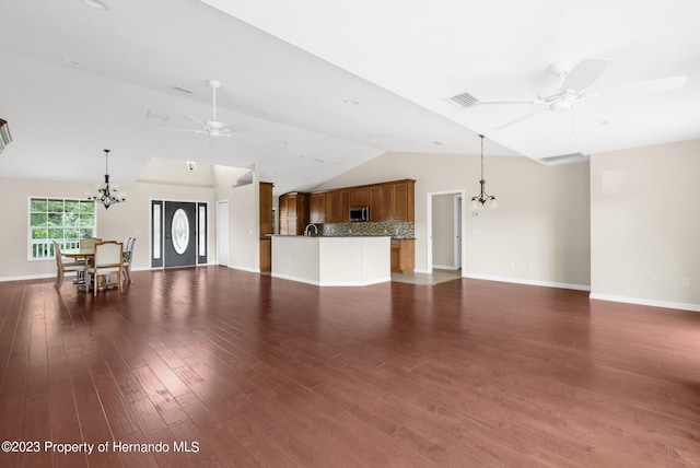 unfurnished living room with ceiling fan with notable chandelier, dark hardwood / wood-style flooring, and vaulted ceiling