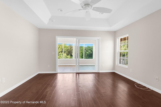 empty room featuring dark wood-type flooring, ceiling fan, and a raised ceiling