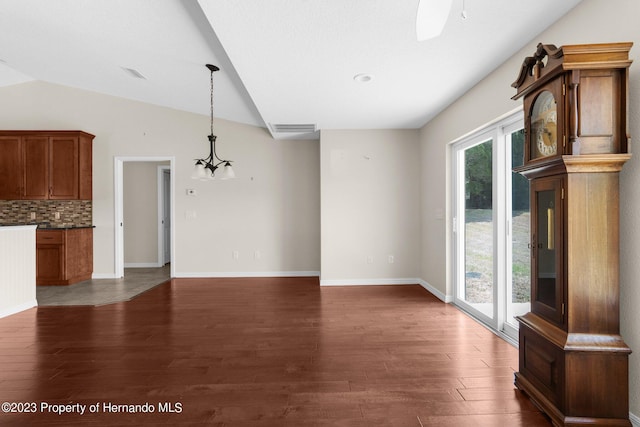 unfurnished living room with dark hardwood / wood-style floors, a chandelier, and vaulted ceiling