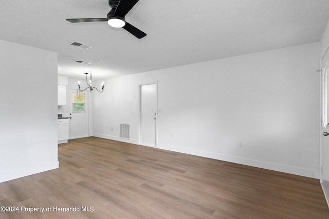 spare room featuring ceiling fan with notable chandelier, light hardwood / wood-style flooring, and a textured ceiling